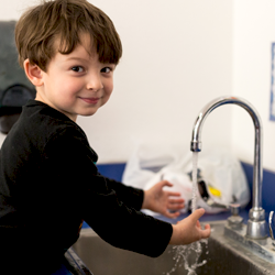 boy washing his hands in sink smiling